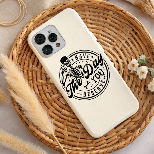 Cream phone case with black skeleton graphic. "Have the Day You Deserve" text. Premium design.