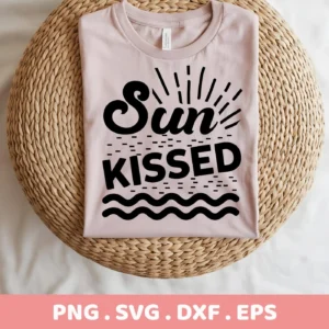 A folded light pink t-shirt with a black "Sun Kissed" SVG design, featuring sun rays, dashes, and wavy lines, displayed on a round woven mat, representing a digital download bundle.
