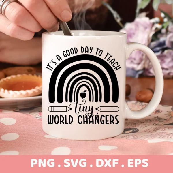Close-up of a white mug featuring a "Teacher Rainbow SVG Design" with the text "It's a good day to teach" above a rainbow graphic and "Tiny World Changers" below, pencils flank the word "tiny," indicating a digital download bundle (SVG, PNG).