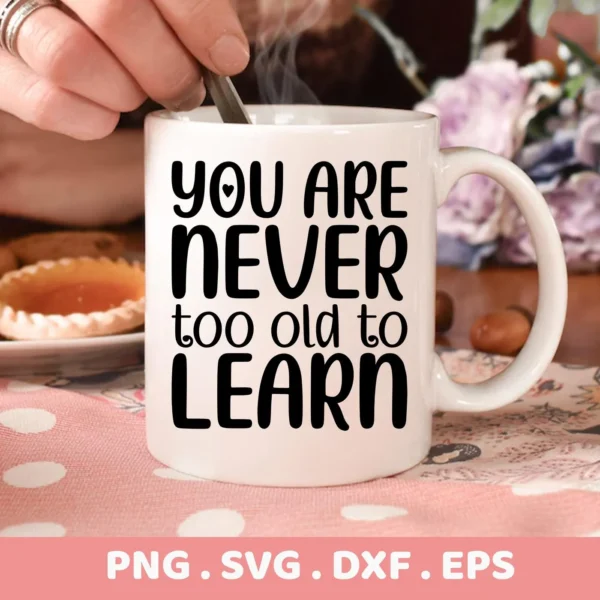 Close-up of a white mug with the text "You Are Never Too Old To Learn" in black lettering, a hand stirring the contents with a spoon, and the file formats PNG, SVG, DXF, and EPS listed below, indicating a digital download bundle.